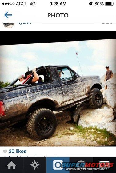 Mud-covered black Ford Bronco with a lifted suspension, off-roading over rocks