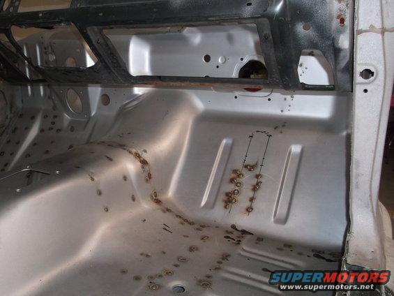 bare metal interior floor pan with some rust spots and weld marks