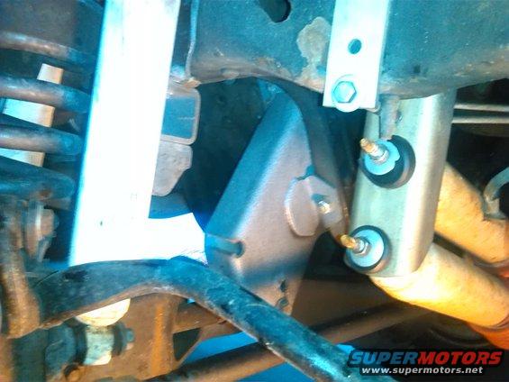 Close-up of a vehicle's rear suspension with shock absorber and springs visible. A metal bracket is attached to the frame