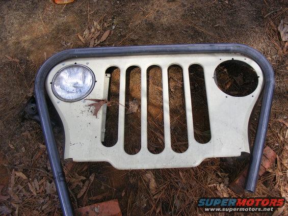 Cream-colored Jeep CJ grille with a chrome roll bar, lying on the ground