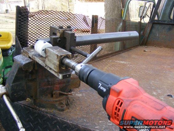 Drill with pipe held in vise on truck bed. Yellow tractor seat visible