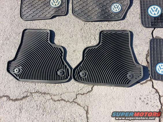 Several black rubber floor mats with Volkswagen logos on a concrete surface