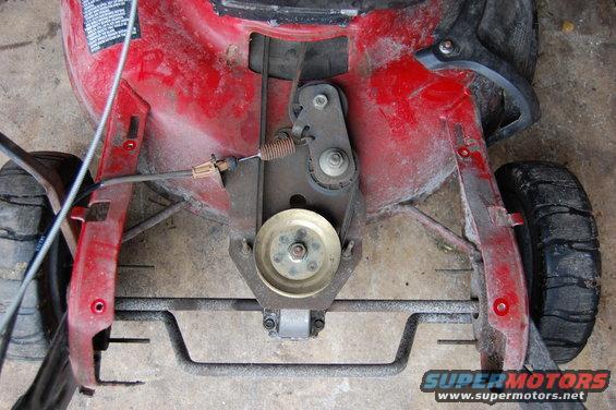 Underside of red lawn mower showing drive belt, pulleys, and rear wheel