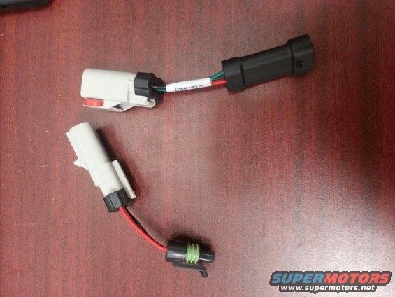 Two wiring harness adapters with white and black connectors on a wooden surface