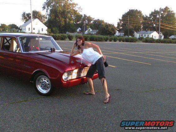 Red 1960 Ford Falcon coupe with a woman leaning on the hood in a parking lot