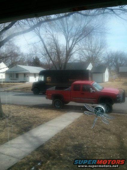 Red pickup truck parked next to a UPS truck on a residential street. Dragonfly lawn ornament in foreground
