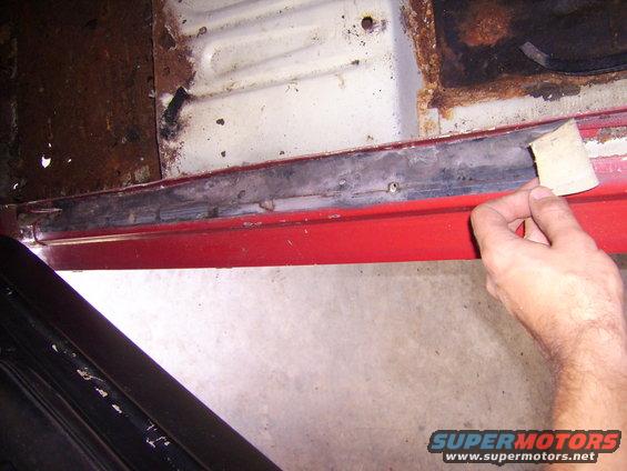 Hand sanding a rusty car door sill. Red paint visible below the sill