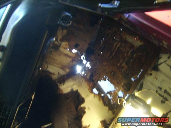 Interior view of a car's floor pan with extensive rust and holes