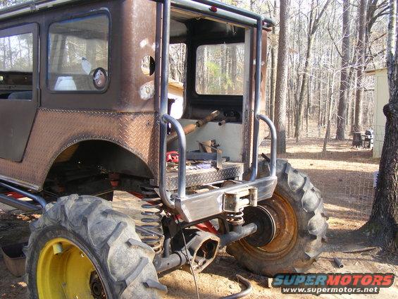 Custom off-road vehicle with diamond plate fenders and large tractor tires, seen from the rear