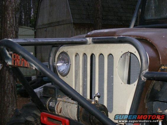 Off-road vehicle grille with vertical slots and a round headlight, protected by a black roll cage