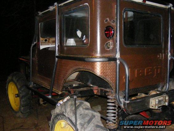 Brown off-road vehicle with large tires and roll cage, rear view