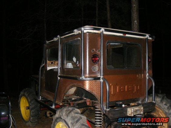 Brown Jeep with yellow wheels and large tires, rear view. Custom roll cage and diamond plate fenders