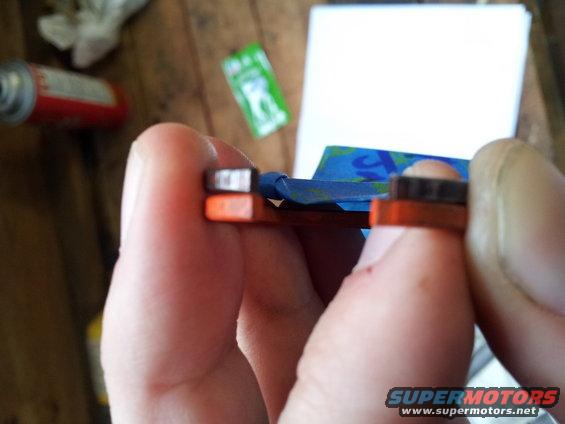 Close-up of hands holding a small orange and black automotive part with blue tape