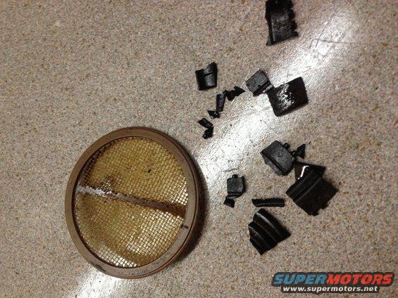 Broken air filter element and scattered black rubber fragments on a speckled surface