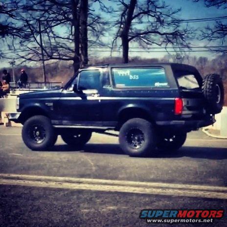 Side view of a dark blue 1995 Ford Bronco with aftermarket wheels and a rear-mounted spare tire
