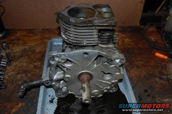 Engine block with fins, crankshaft visible, sitting in a gray tray with oil