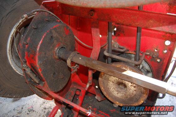 Red lawn mower axle assembly with grease and dirt, showing a tire, brake drum, and drive belt