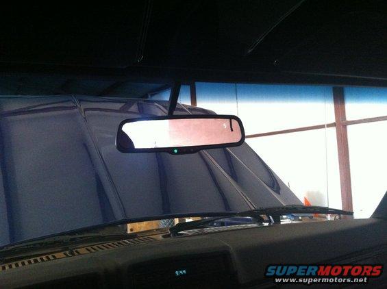 Interior view of a car's dashboard and rearview mirror, with a blue tarp covering the hood