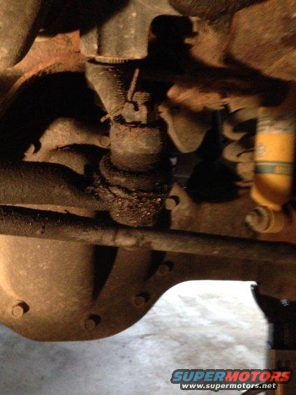 Close-up of rusty suspension parts, including a ball joint and tie rod, with a yellow shock absorber visible