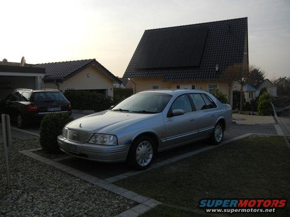 1999 Ford Fairlane sedan parked in driveway next to a dark SUV