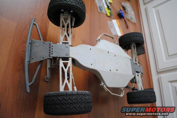 RC car chassis with suspension and tires, parts on wall behind