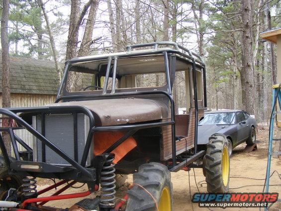 Custom off-road vehicle with large tractor tires, roll cage, and a dark sedan behind it
