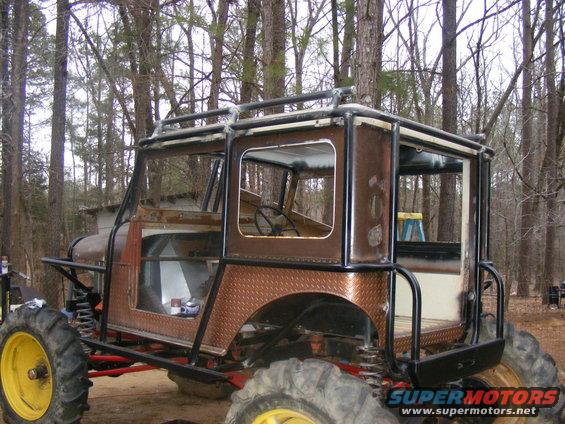 Custom buggy with roll cage, diamond plate fenders, and large tires, parked in woods