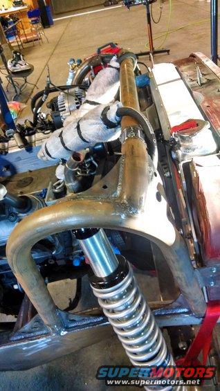 Vehicle chassis with exposed engine, roll cage, and a coilover shock absorber. Some parts are wrapped in insulation