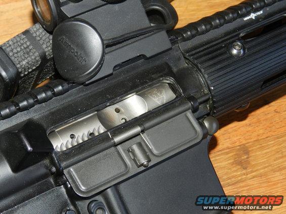 Close-up of AR-15 rifle receiver with Aimpoint optic. Shows bolt carrier group and charging handle