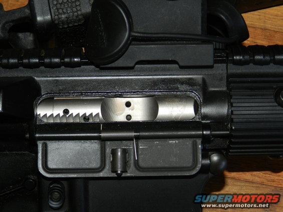 Close-up of a firearm receiver with visible bolt carrier group and serrated edge