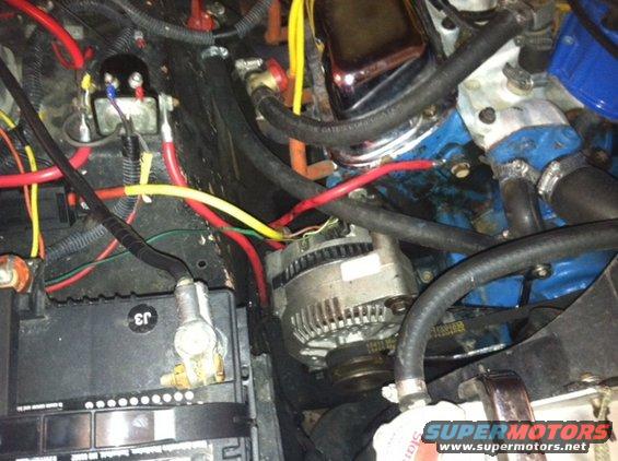 Close-up of a vehicle's engine bay with battery, alternator, and wiring visible