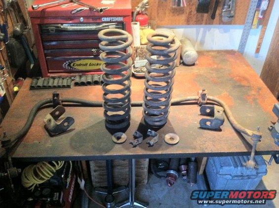 Two front coil springs and sway bar components on a workbench