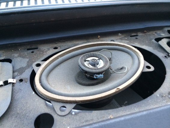 Car speaker mounted in a dashboard opening, showing dust and wear