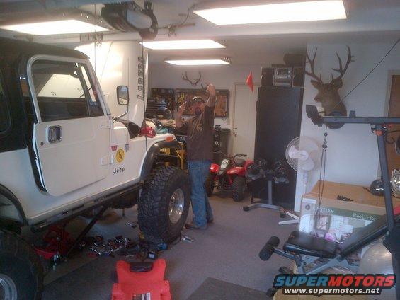 White 1985 Jeep CJ7 with black top, lifted suspension, and large tires in a garage. A person stands next to it