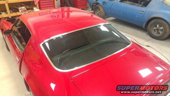Red coupe with chrome trim around rear window, seen from a high rear angle