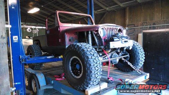 Jeep CJ-series on trailer, lifted by shop equipment. Modified with large tires and off-road suspension