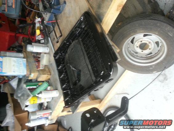 Black seat frame on sawhorses next to a tire and various cans