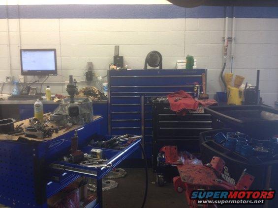 Mechanic's bay with tool chests, computer monitor, and car parts on workbench