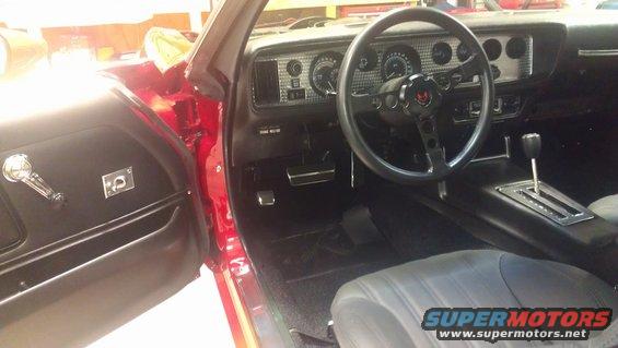 Interior shot of a red car, showing the dashboard, steering wheel with a bird emblem, center console with automatic shifter, and part of the driver's seat