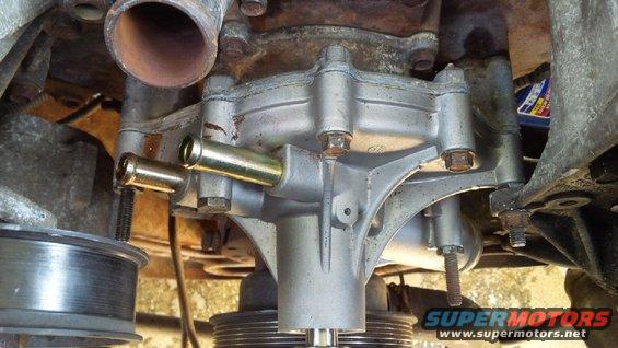 Engine water pump with two brass hose fittings, showing corrosion and some fluid residue