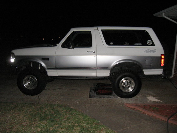 White and silver Ford Bronco with lifted suspension and aftermarket wheels, seen from the side