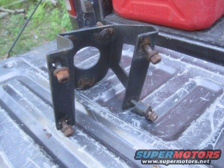 Black metal bracket with rusty bolts on a truck bed, next to a red gas can