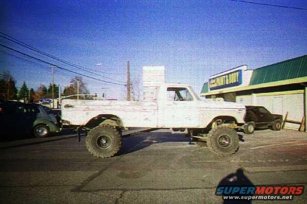 Lifted white pickup truck parked outside a store, with a dark SUV behind it