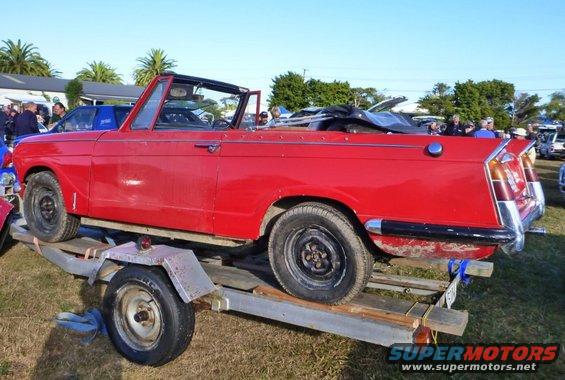 Red convertible car on a trailer, side view, with a black soft top folded in the back