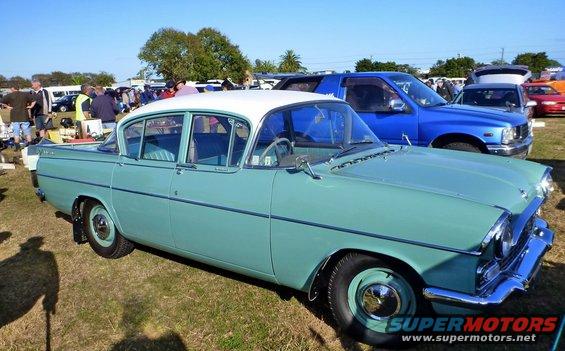 Turquoise and white sedan with chrome accents parked on grass, front quarter view