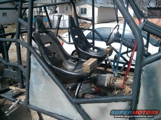 Off-road buggy interior with bucket seats, roll cage, and steering wheel. Visible text: SUPERMOTORS