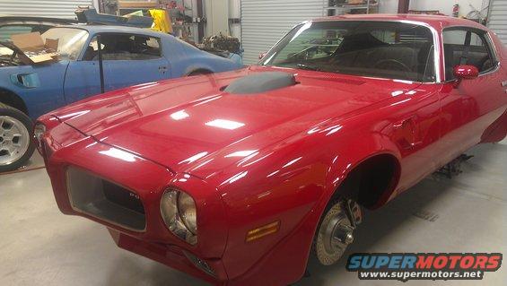 red muscle car with hood scoop, another blue car behind it in a garage