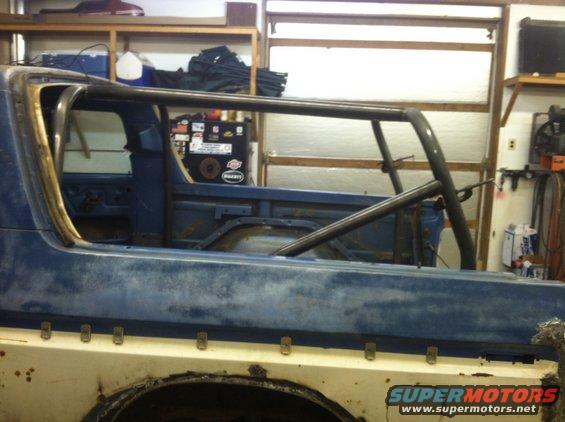 Side view of a 1979 Ford Bronco with a roll cage installed, in a workshop