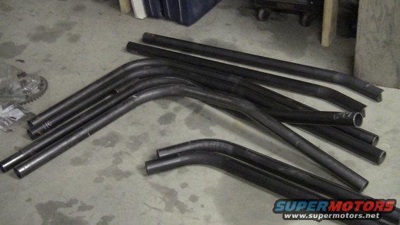 Metal tubing bent into various curves and straight sections lies on a concrete floor