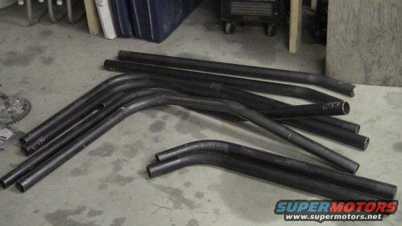 Pile of bent black metal tubes on a concrete floor. Some have markings